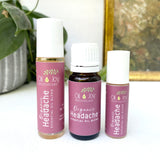 Three bottles of Organic Headache Essential Oil Blend by Oil Joy Apothecary on a white surface with a plant and gold frame in the background.