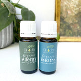 Two essential oil bottles labeled 'Allergy' and 'Breathe' from Oil Joy Apothecary on a white surface with a plant in the background.