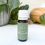 Bottle of Organic Majoram oil from Oil Joy Apothecary on a white surface with plants in the background
