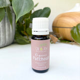 Bottle of Organic Patchouli oil from Oil & Joy Apothecary on a white surface with greenery in the background.