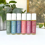 Set of six roller bottles with various labels on a white surface with greenery in the background