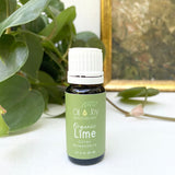 Bottle of Organic Lime essential oil from Oil of Joy Apothecary on a white surface with green leaves in the background.