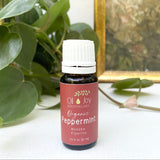 Bottle of Organic Peppermint essential oil from Oil Joy Apothecary on a white surface with green leaves in the background.