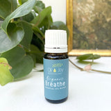 Bottle of 'Organic Breathe' essential oil blend by Oil Joy Apothecary on a white surface with green leaves in the background.