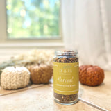 Jar of 'Harvest' organic tea blend on a surface with decorative pumpkins in the background.