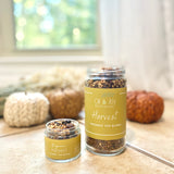 Two jars of 'Harvest Organic Tea Blend' by Oil & Joy Apothecary on a surface with pumpkins in the background.