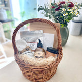 Postpartum gift basket with various items including a candle, lotion, soup, bath soak, and healing products on a light surface.