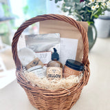 Postpartum gift basket with various items including a candle, lotion, soup, bath soak, and healing products on a light surface.