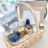 Postpartum gift basket with various items including tea, lotion, soup, bath soak, and healing products on a light surface.