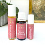 Three bottles of 'Good Morning' essential oil blends from Oil Joy Apothecary on a white surface with a plant and gold frame in the background.