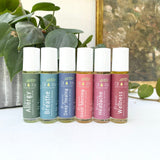 Set of six roller bottles with various labels on a white surface with greenery in the background