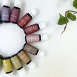 Assorted essential oil bottles arranged in a circular pattern on a white background with green leaves.