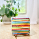 Colorful striped cherry pit therapy pack in clear packaging on a light surface with a blurred plant in the background