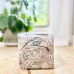 Floral-patterned cherry pit therapy pack on a wooden surface with a blurred green plant in the background