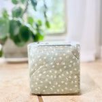Green cherry pit therapy pack with white polka dots on a wooden surface with a blurred plant in the background