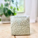 Green cherry pit therapy pack with white polka dots on a wooden surface with a blurred plant in the background