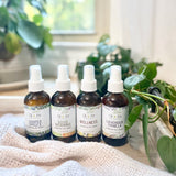 four bottles of Oil of Joy essential oil fragrance sprays on a wooden surface with plants in the background.