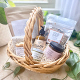 Postpartum gift basket with natural products including tallow lotion, soup mix, essential oil candle, herbal balm and sitz bath.