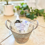 Bath products in a decorative metal bucket with plants in the background