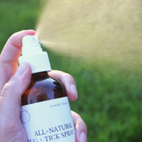 Hand holding a bottle of all-natural bug and tick spray with grass in the background